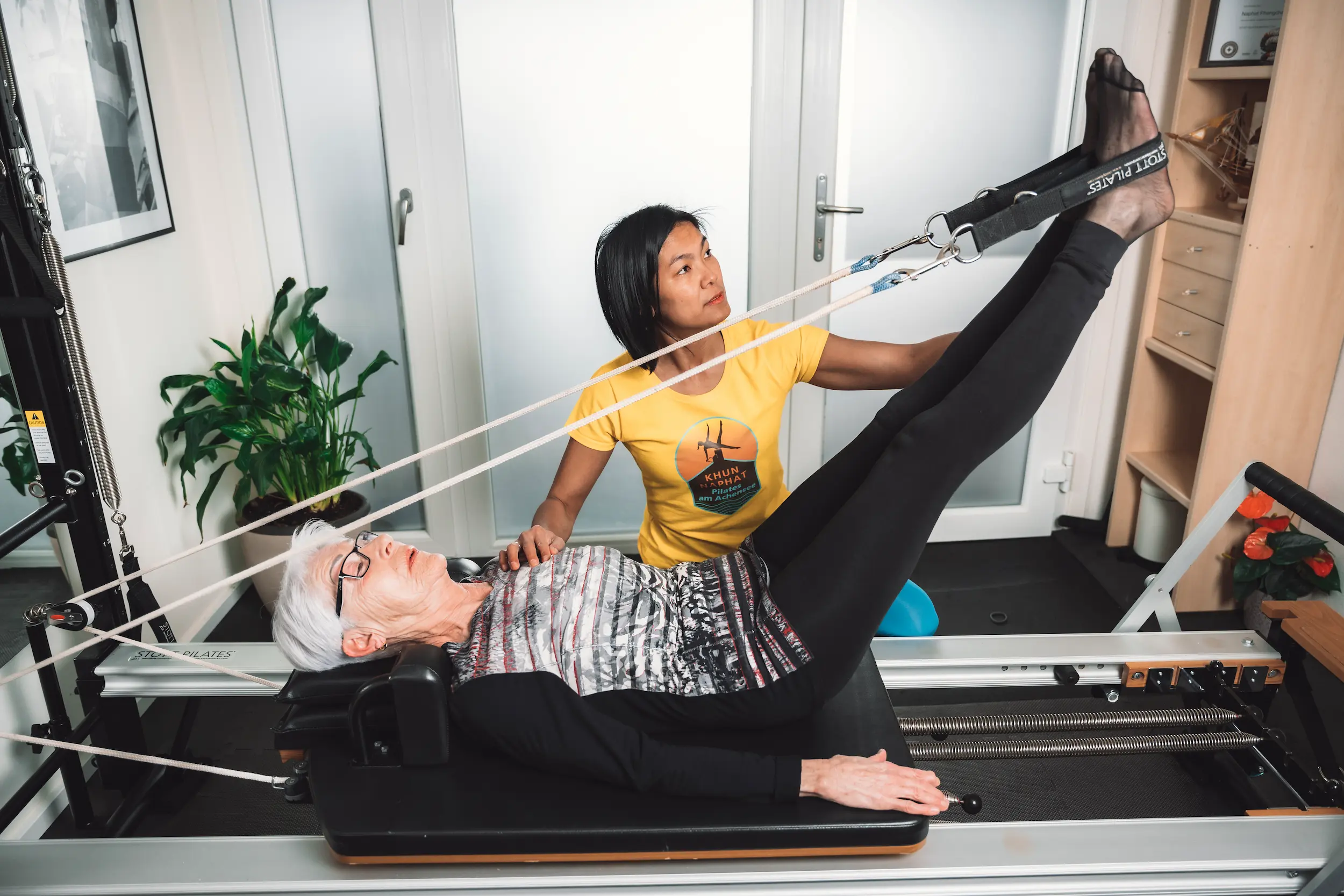 Pilates-Trainerin unterstützt Seniorin bei Beinübung am Reformer in Maurach am Achensee