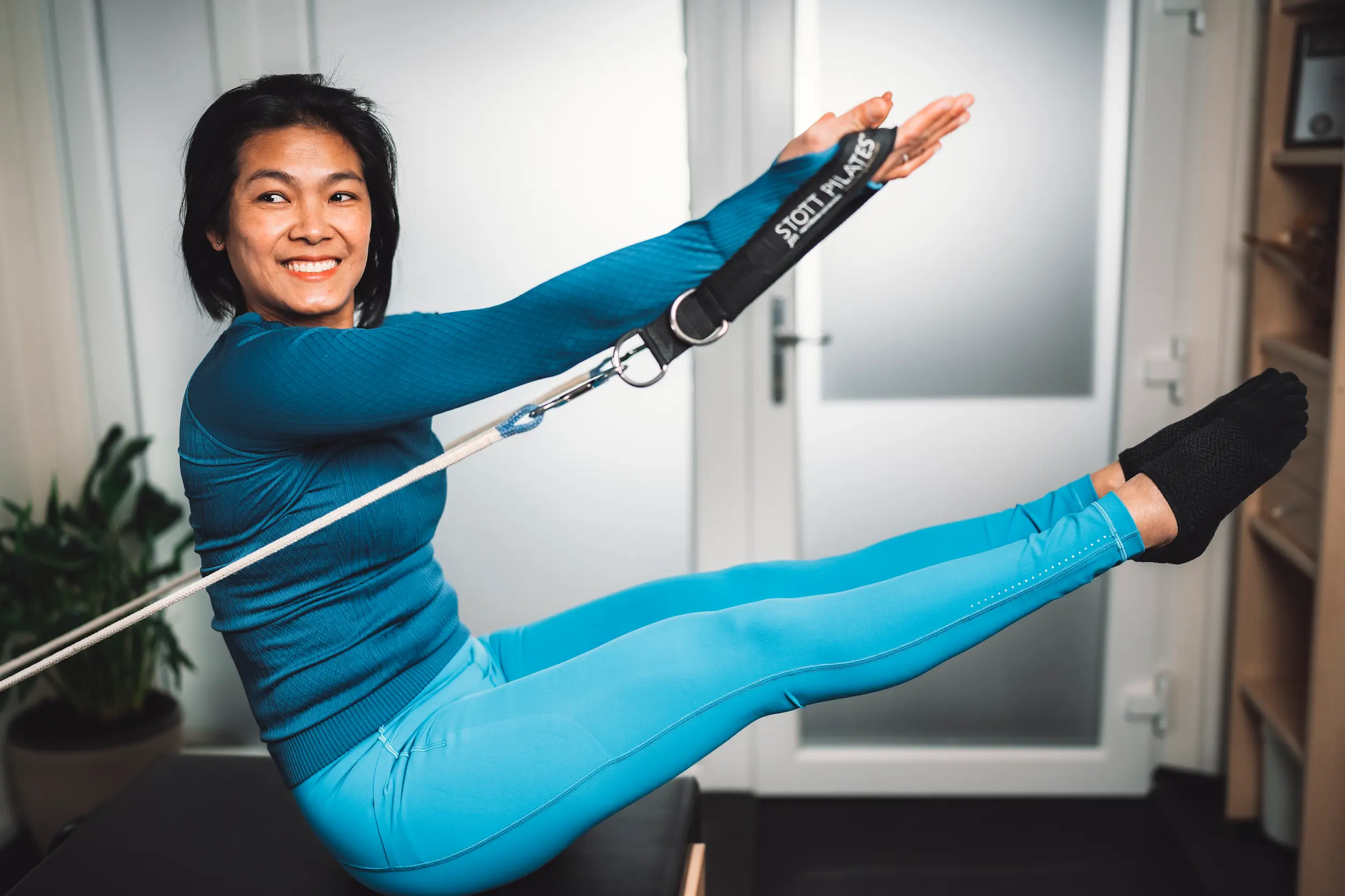 Reformer Pilates-Training: Eine Trainerin führt die fortgeschrittene 'Teaser'-Position mit Gurten aus.